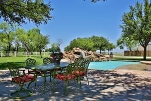 backyard patio,and table with rock waterfall pool, white picket fence, and pastures in the background